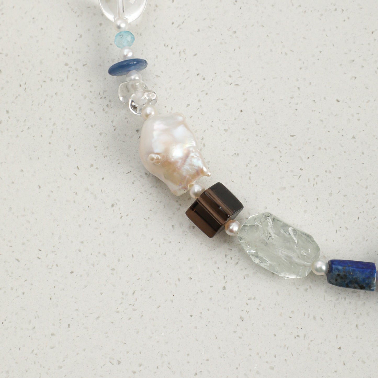 Lapis lazuli necklace detail: pearl and blue stones with a clear faceted crystal segment
