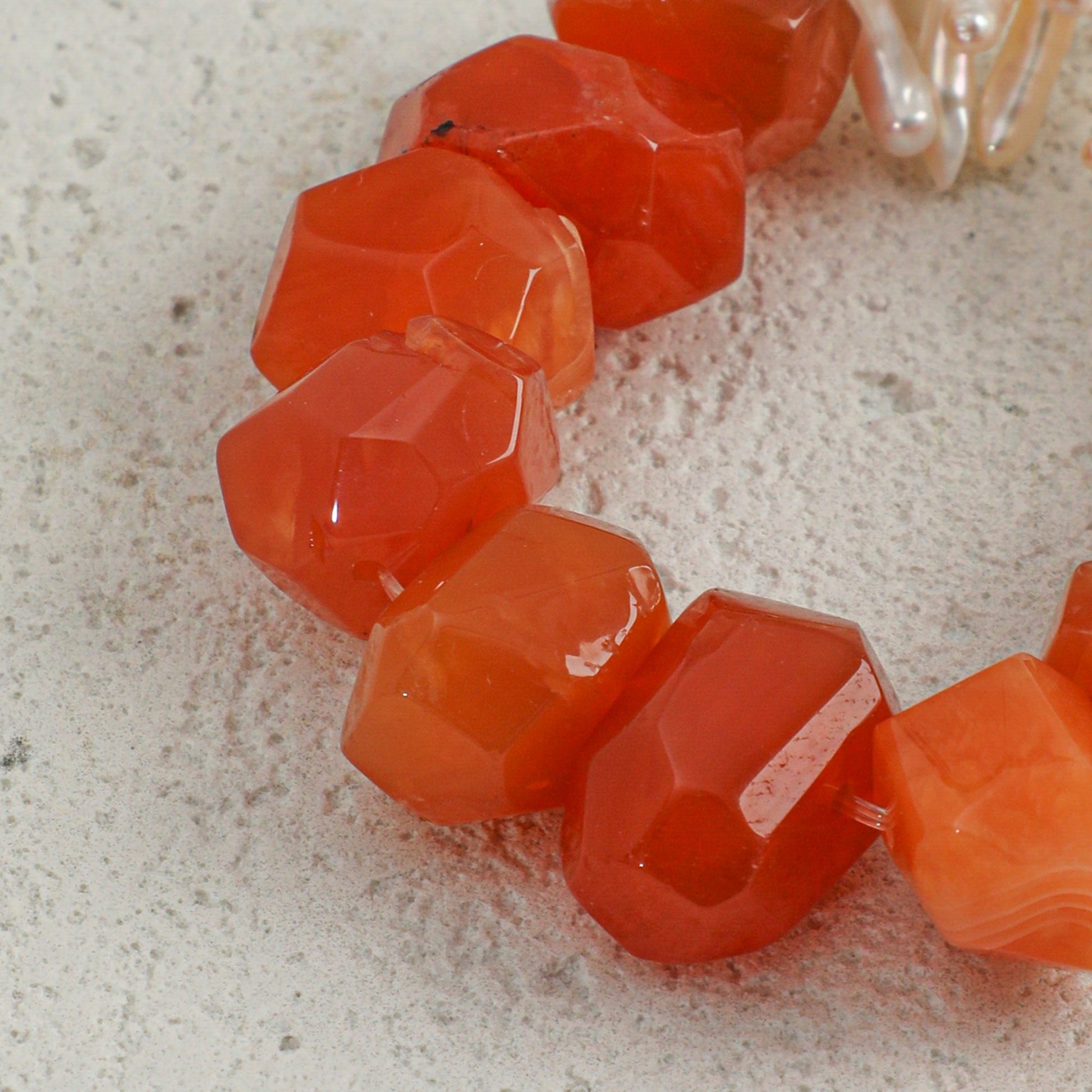 Faceted orange-red agate beads on a bracelet strand with white pearl accents