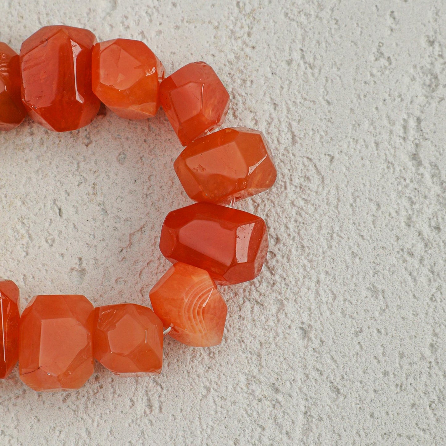 Orange-red faceted agate beads on bracelet with visible links between stones
