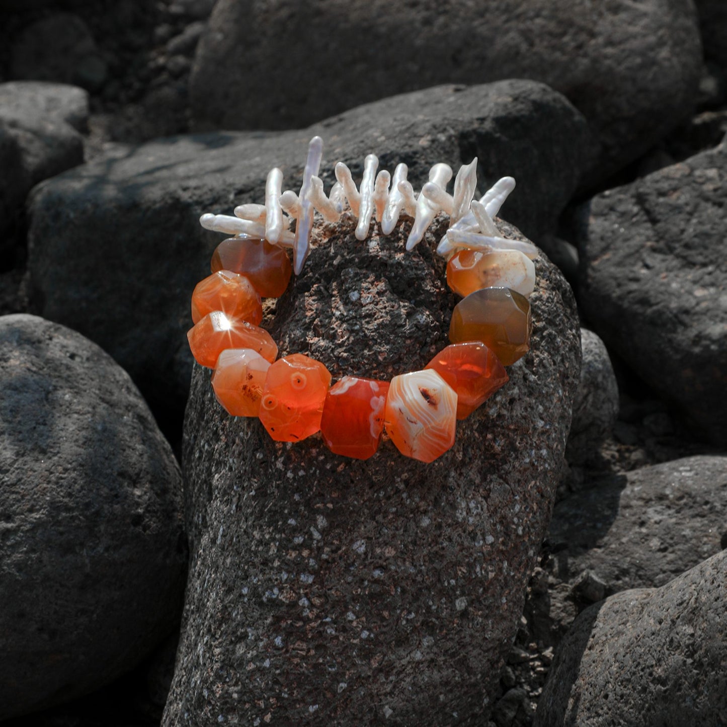 Bracelet with orange agate beads and white pearl-like accents on dark rocks