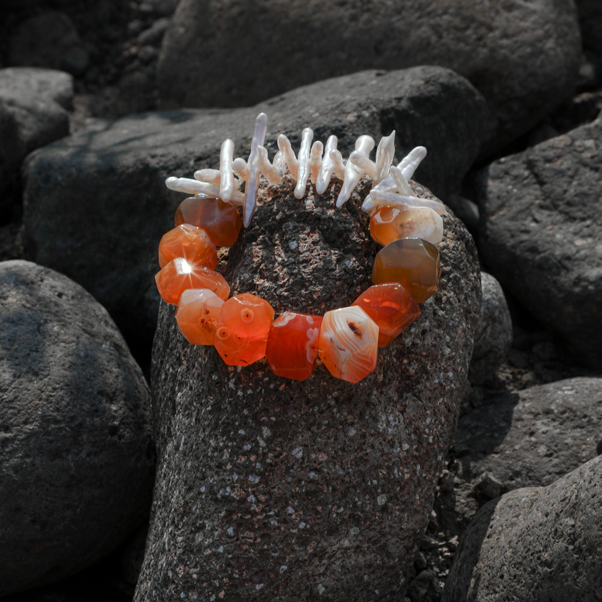 Bracelet with orange agate beads and white pearl-like accents on dark rocks