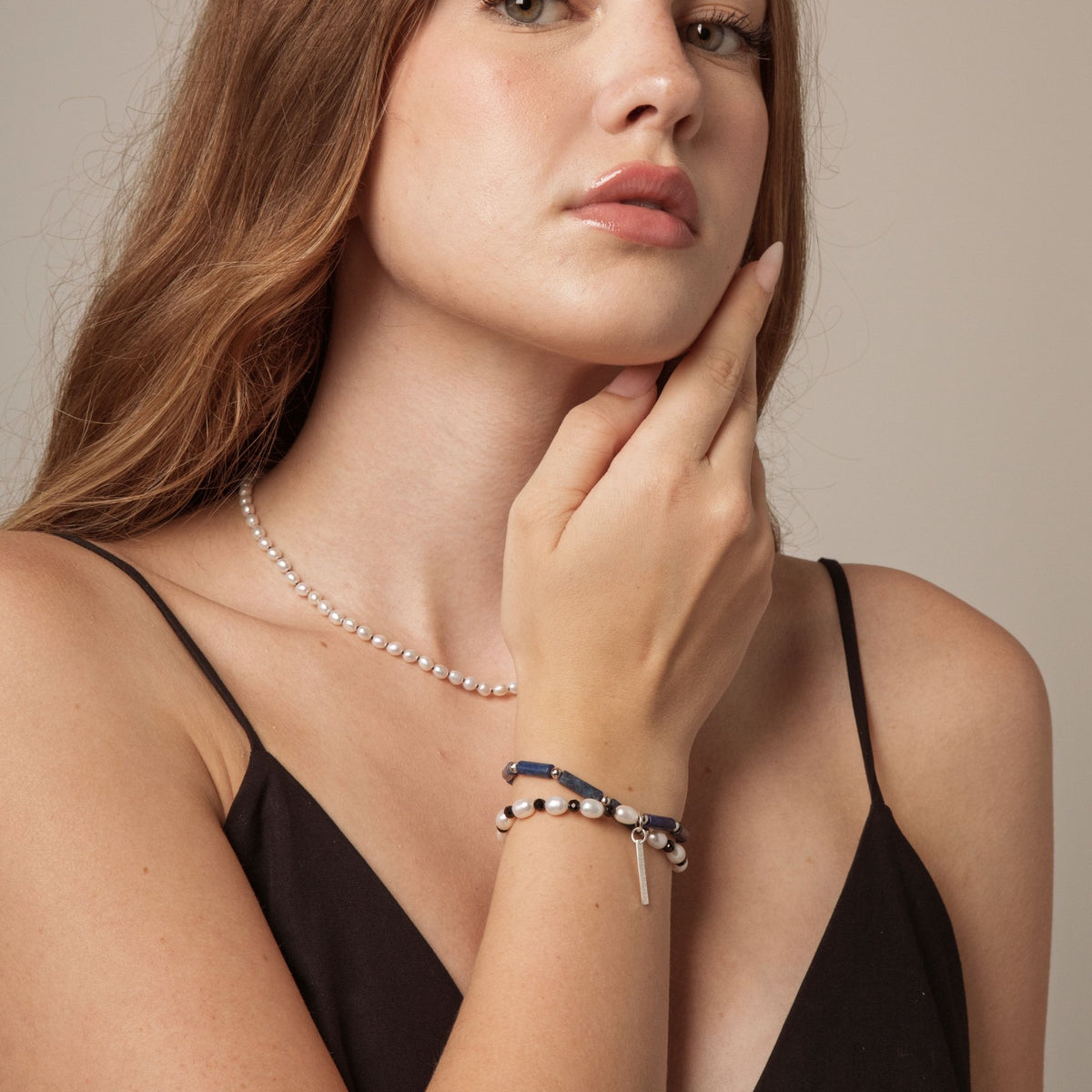 Beaded bracelet on wrist with white pearls, blue lapis, and black accents
