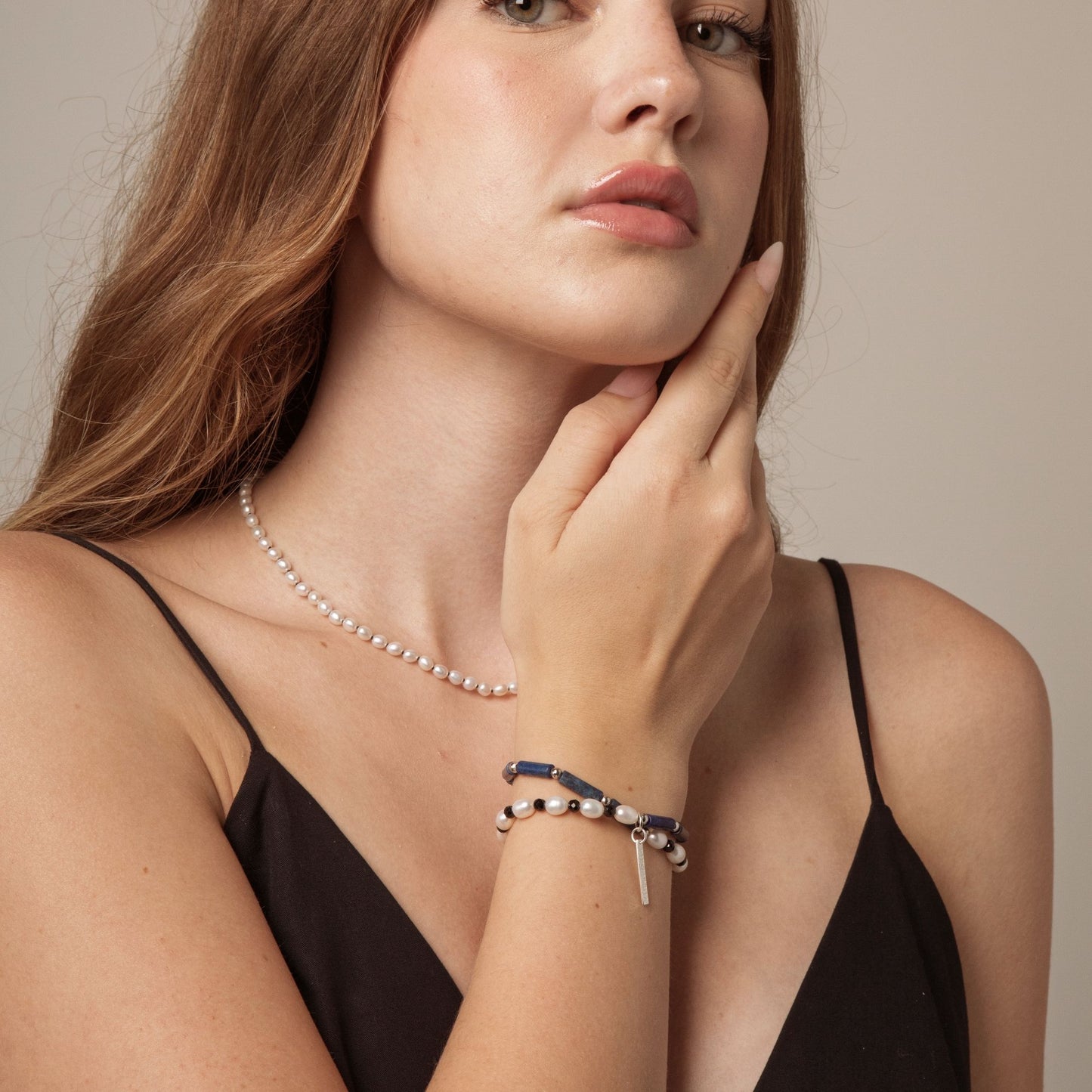 Beaded bracelet on wrist with white pearls, blue lapis, and black accents