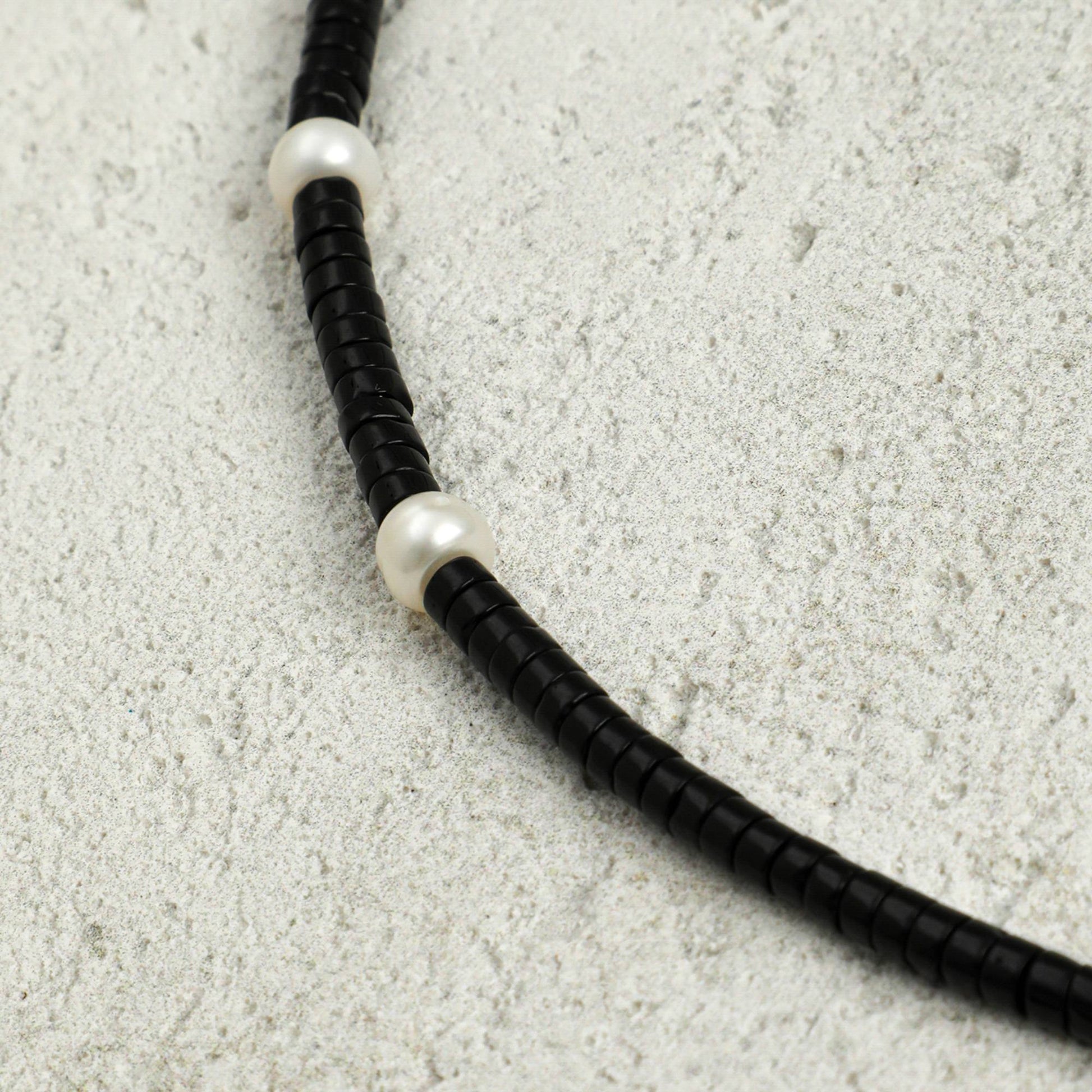 Black cord necklace detail with white pearl-like spacers along the braided strand