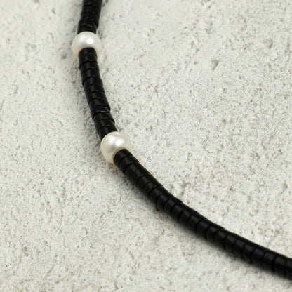 Black cord necklace detail with white pearl-like spacers along the braided strand