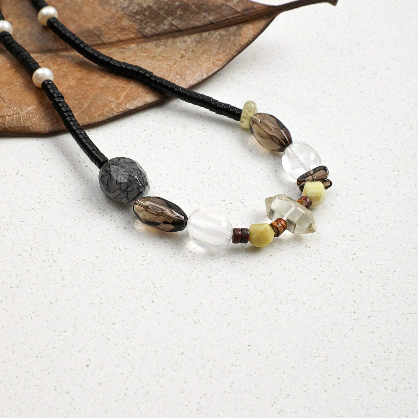 Black cord necklace with grey stones, white crystals, and gold-tone bead accents